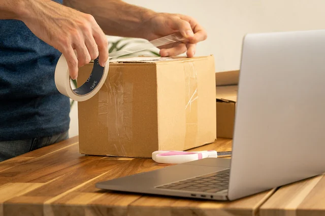 Preparazione di un pacco con nastro adesivo accanto a un computer portatile